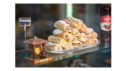 Stacked pastry rolls dusted with powdered sugar displayed on a white plate behind a glass bakery counter.