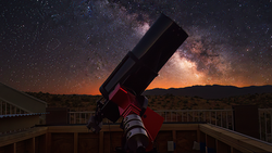Red and black telescope pointed upward at night sky filled with stars and Milky Way.