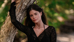 Woman in black top leaning against tree trunk in outdoor setting.