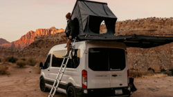 White van with open roof tent in desert landscape during golden hour.