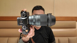 Photographer holding a vintage film camera with a large telephoto lens attached, positioned to obscure their face.