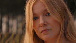 Woman with long reddish-blonde hair gazing downward with a contemplative expression.