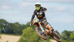 Motocross rider airborne on dirt bike mid-jump against cloudy sky.