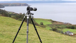 Camera mounted on tripod overlooking coastal landscape with mountains and water.