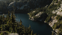 Alpine lake surrounded by dense evergreen forest and rocky granite peaks under bright daylight.
