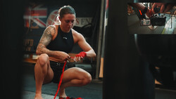 Athlete in black tank top performing a squat with a red resistance band in a gym.