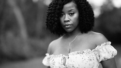 Black and white portrait of a woman with textured curly hair wearing an off-shoulder white lace top.