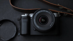 Mirrorless camera with prime lens, lens cap, and brown leather strap on dark surface.