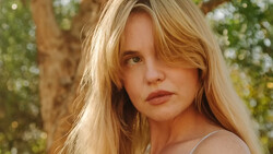 Young woman with long blonde hair gazing over shoulder in natural outdoor setting.