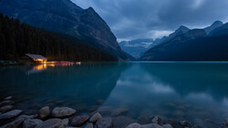 Mountain lake at twilight with illuminated boathouse reflected in perfectly still turquoise water.