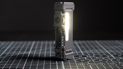 Compact tactical flashlight with integrated controls illuminated against a dark grid surface.