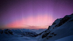 Snow-covered alpine valley at twilight with purple and pink aurora-like sky above distant mountains.