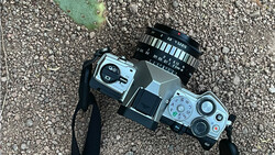 Vintage rangefinder film camera with black lens mounted on gravel surface.