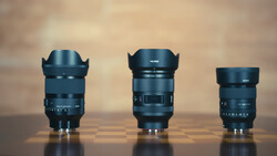 Three camera lenses of varying sizes arranged side by side on a reflective surface against a warm, blurred background.