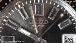 Close-up macro photograph of a Seiko Automatic watch face with dark dial and applied hour markers.