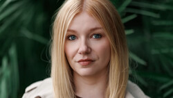 Portrait of a woman with straight blonde hair against blurred green foliage background.