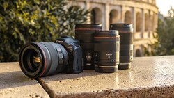Canon EOS R5 camera with RF mount lens surrounded by three additional Canon RF lenses on stone surface.