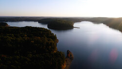 Aerial view of a forested landscape with multiple lakes and a prominent rocky outcrop in the foreground at golden hour.