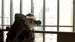 Photographer shooting with a telephoto lens from a high-rise window overlooking a city skyline.