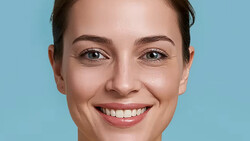 Woman with warm smile looking directly at camera against blue background.