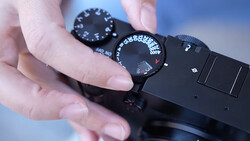 Close-up of a photographer's hand adjusting the exposure compensation dial on a black camera body.