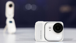 White compact camera with articulating lens and rectangular design, shown against dark background.