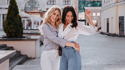 Two women posing together in an urban courtyard with classical architecture in the background.