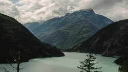 Alpine lake with turquoise water surrounded by forested mountains and dramatic cloudy sky.