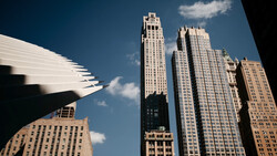 Upward view of modern and historic skyscrapers against a bright blue sky with white clouds.