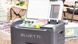 Bluetti portable power station with open lid displaying control panel and battery display outdoors.