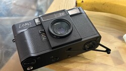 Lomo compact film camera with textured black body and manual controls positioned on wooden surface.