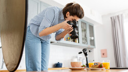Photographer composing a still life shot of kitchen items on a wooden table using a professional camera.