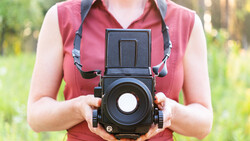 Photographer holding a medium format camera with flip-up viewfinder against their body.