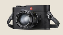 Leica rangefinder camera with textured black body and fixed lens, shown with attached shoulder straps against neutral background.