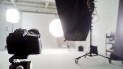 DSLR camera on tripod positioned in studio with bright LED panel lights and reflectors in background.
