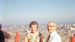 Two people standing on an elevated observation deck overlooking a sprawling cityscape at dusk.