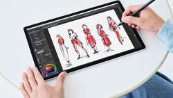 Designer using stylus on tablet displaying fashion figure sketches in red.