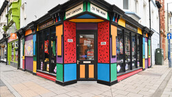 Vibrant corner storefront with bold primary colors, geometric patterns, and black framing on a brick street.