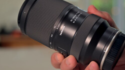 Telephoto zoom lens held in hands, showing focus and aperture rings with distance scale markings.