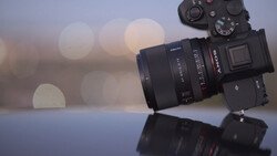 Sony mirrorless camera with attached lens positioned on reflective surface against blurred bokeh background.