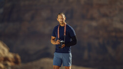 Male runner jogging outdoors at dusk wearing navy shirt, blue shorts, and a medal around his neck.