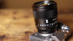 Telephoto lens mounted on vintage rangefinder camera body against wooden surface.