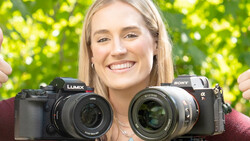 Woman holding a Lumix mirrorless camera in one hand and a Sony Alpha mirrorless camera in the other against a bright green bokeh background.