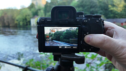 Mirrorless camera mounted on a tripod displaying a river landscape on its rear LCD screen.