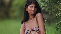 Woman in floral dress posing against blurred green foliage background.