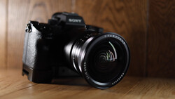 Sony mirrorless camera with wide-angle lens on wooden surface under warm studio lighting.