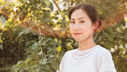 Woman in light-colored lace top poses among foliage during golden hour.