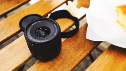 Black telephoto lens with lens hood on wooden surface next to white plate with food.