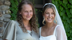 Two women smiling at camera, one wearing a white bridal veil and dress, the other in a light gray sleeve dress.