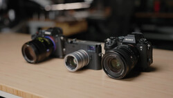 Three mirrorless cameras arranged on a wooden table, displaying different lens and body configurations.